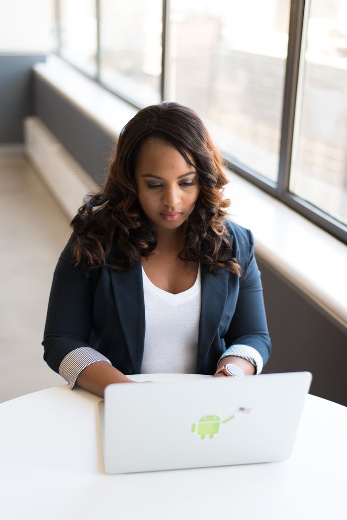 African American woman focused on laptop in a modern office setting with natural light.