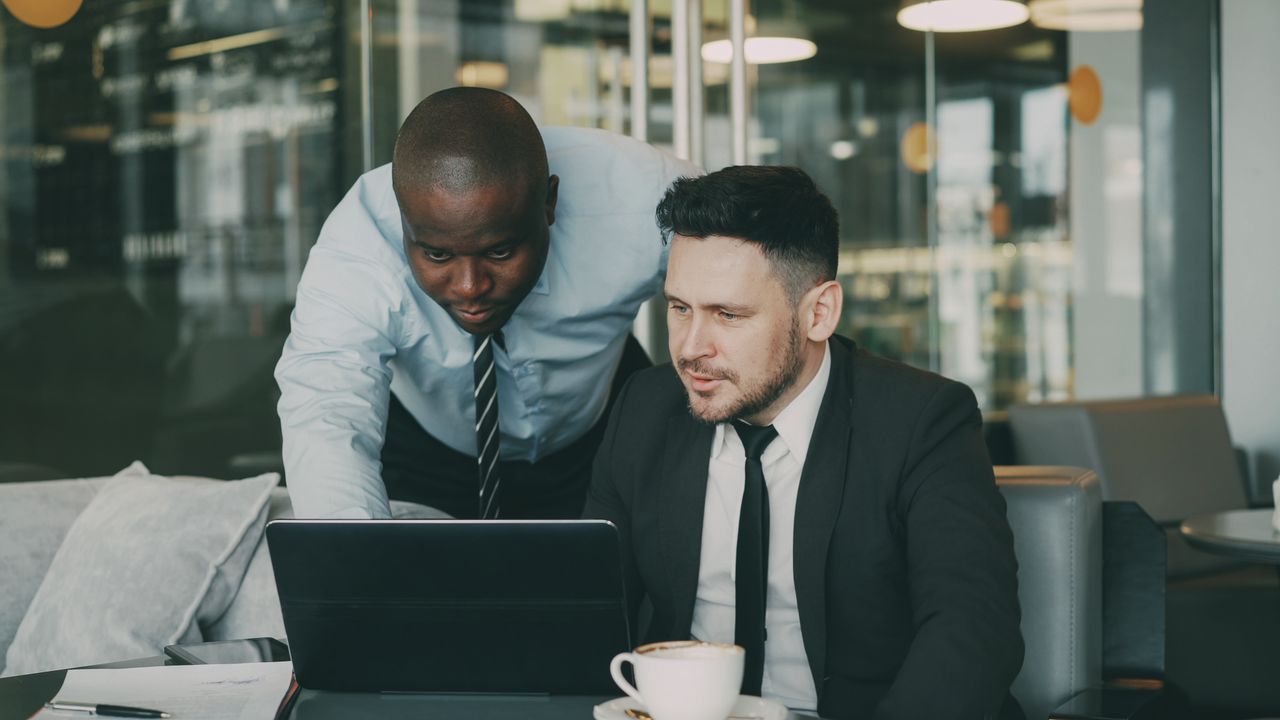 Two business professionals engaged in a collaborative discussion using a laptop in a modern office.